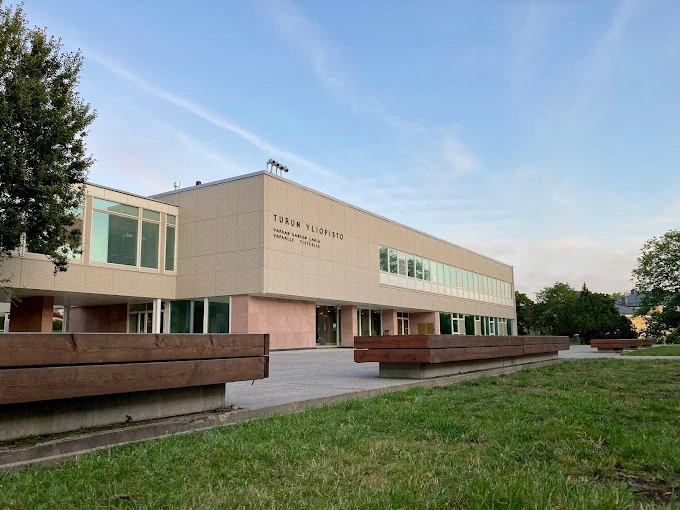 Turku Üniversitesi Modern Kampüs Binası Turku Üniversitesi, Finlandiya’nın en köklü eğitim kurumlarından biri olarak modern kampüs yapılarıyla dikkat çekmektedir. Fotoğrafta, üniversitenin çağdaş mimariye sahip fakülte binası, geniş cam pencereleri ve öğrenciler için düzenlenmiş açık alanıyla görülmektedir. Turku Üniversitesi, öğrencilere hem akademik hem de sosyal açıdan ilham verici bir ortam sunmaktadır.