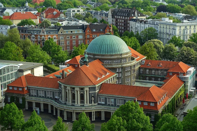 Hamburg Üniversitesi Tarihi Kampüs Binası Hamburg Üniversitesi, Almanya’nın en köklü eğitim kurumlarından biri olarak modern eğitim anlayışını tarihi kampüs binasıyla birleştiriyor. Kırmızı çatılı görkemli yapısı ve etkileyici kubbesiyle öne çıkan bu üniversite, Hamburg’un merkezinde öğrencilere akademik başarı ve kültürel çeşitliliği bir arada sunmaktadır.