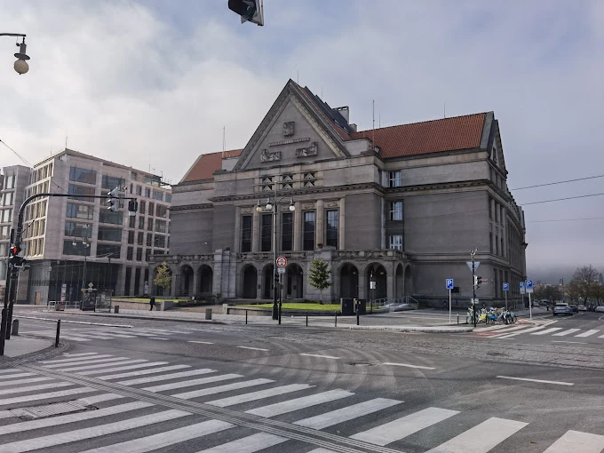 Charles Üniversitesi, Prag’ın merkezinde yer alan tarihi binalarıyla Avrupa’nın en prestijli eğitim kurumlarından biridir. Fotoğrafta üniversitenin klasik mimari tarzını yansıtan taş yapısı, üçgen alınlıklı cephesi ve kırmızı kiremitli çatısı görülmektedir. Çevresindeki modern yapılar ve geniş caddeler, Charles Üniversitesi’nin hem tarihi hem de çağdaş bir şehir dokusu içinde konumlandığını göstermektedir.