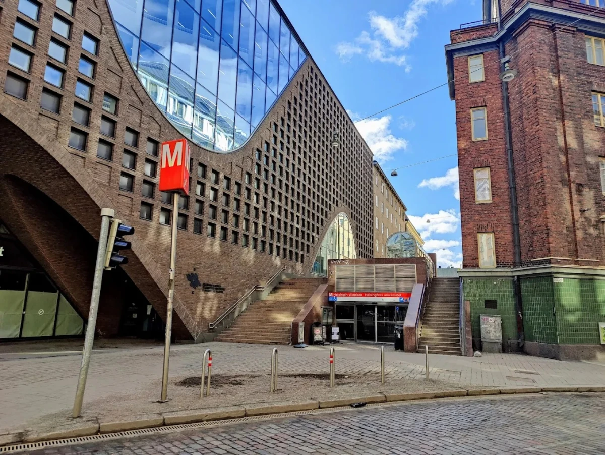 Helsinki Üniversitesi Metro Girişi ve Modern Mimari Helsinki Üniversitesi, şehir merkezinde yer alan modern mimarisiyle dikkat çeken kampüs yapıları ve metro istasyonu girişleriyle öne çıkıyor. Fotoğrafta, üniversitenin cam ve tuğla detaylarla tasarlanmış ikonik binası ile Helsinki Üniversitesi metro durağı görülmektedir.