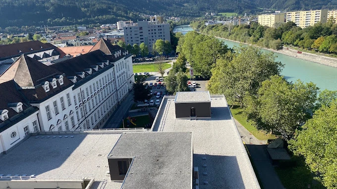 Innsbruck Üniversitesi Kampüsü Innsbruck Üniversitesi kampüsü, Alplerin eteklerinde yer alan doğal güzellikleri ve tarihi yapılarıyla dikkat çekmektedir. Fotoğrafta üniversitenin tarihi binaları, modern yapılar ve hemen yanında uzanan nehir görülmektedir. Innsbruck Üniversitesi, doğa ile iç içe konumu sayesinde öğrencilere hem akademik hem de yaşam kalitesi açısından eşsiz bir ortam sunmaktadır.