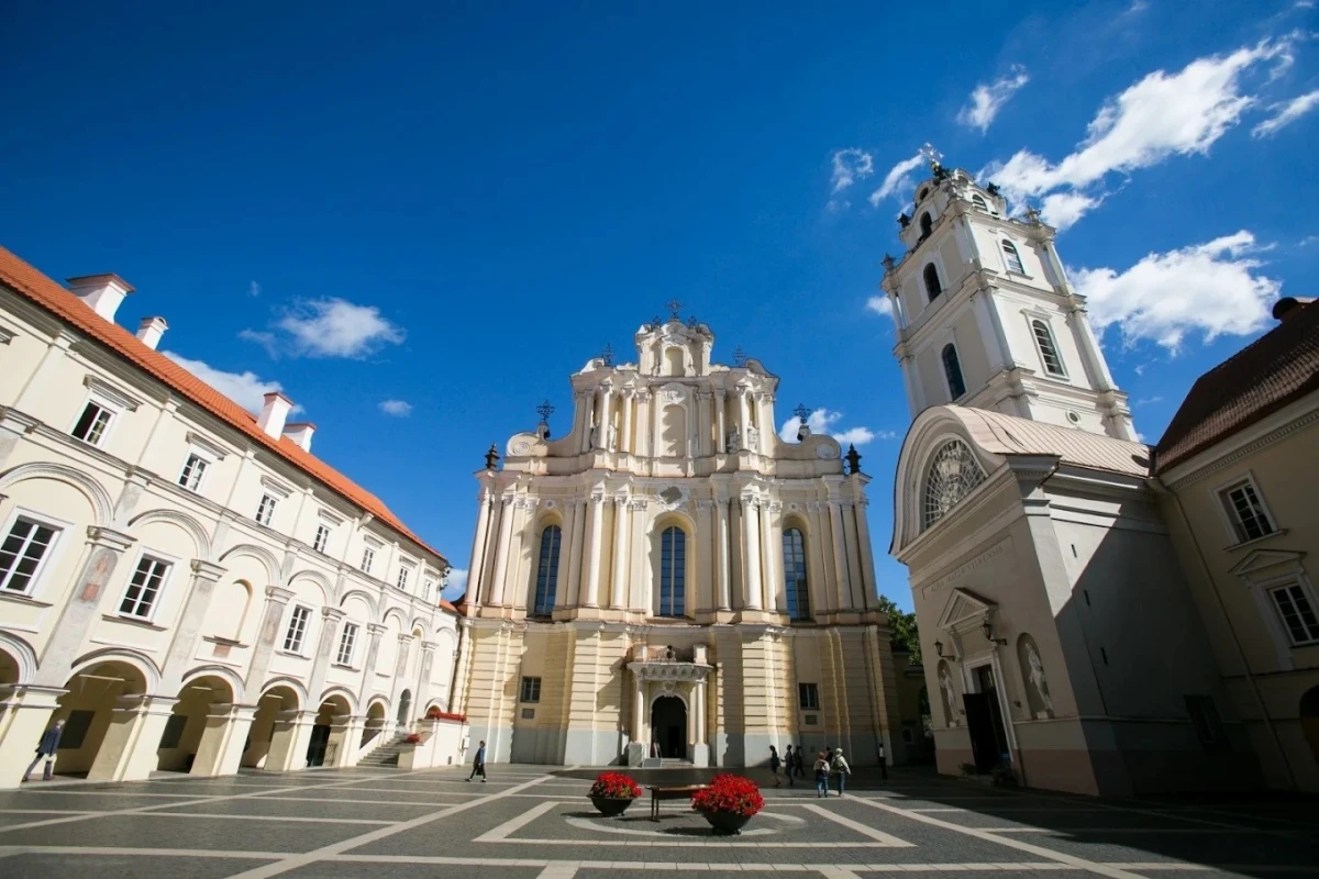 Vilnius Üniversitesi Tarihi Kampüs ve Barok Mimari Vilnius Üniversitesi, Litvanya’nın başkenti Vilnius’ta yer alan ve Avrupa’nın en köklü üniversitelerinden biridir. Fotoğrafta üniversitenin barok mimari tarzıyla inşa edilmiş tarihi ana binası ve zarif çan kulesi görülmektedir. Geniş avlusu, zarif sütunları ve tarihi dokusuyla Vilnius Üniversitesi, hem akademik başarıları hem de mimari güzelliğiyle dikkat çeken prestijli bir eğitim kurumudur.