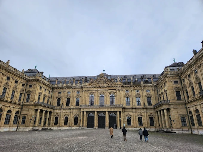 Würzburg Üniversitesi Tarihi Kampüs Binası Würzburg Üniversitesi, Almanya’nın en köklü eğitim kurumlarından biri olarak tarihi dokusuyla öne çıkıyor. Fotoğrafta, barok mimarisiyle dikkat çeken üniversitenin tarihi kampüs binası yer almakta. Geniş avlusu, zarif detaylara sahip taş işçiliği ve ihtişamlı tasarımıyla Würzburg Üniversitesi, hem öğrenciler hem de ziyaretçiler için etkileyici bir atmosfer sunuyor.