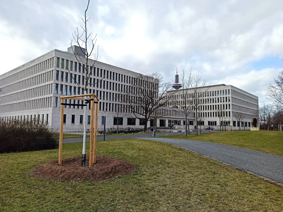 Goethe Üniversitesi Modern Kampüs Binası Goethe Üniversitesi, Almanya’nın finans ve kültür başkenti Frankfurt’ta yer alan, modern yapıları ve güçlü akademik programlarıyla tanınan prestijli bir eğitim kurumudur. Fotoğrafta, üniversitenin modern tasarımlı kampüs binası, geniş yeşil alanlar ve arka planda Frankfurt’un simgesi olan televizyon kulesi dikkat çekiyor.