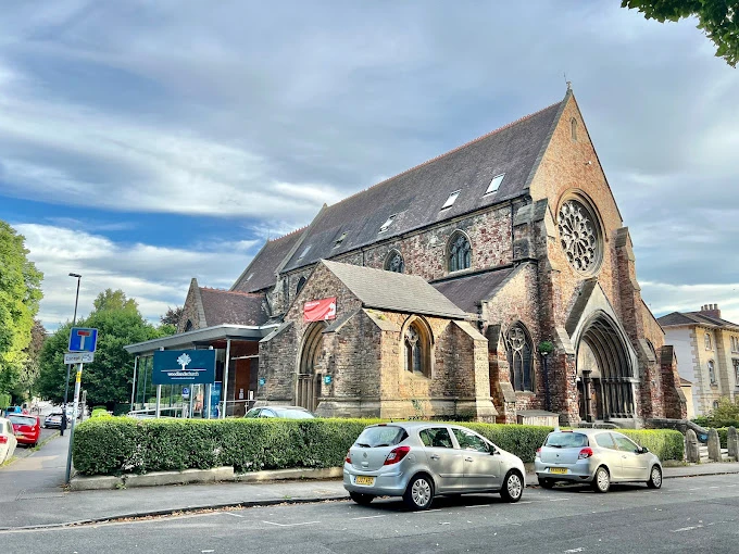 Bristol Üniversitesi Tarihi Taş Binası ve Çevresi Bristol Üniversitesi’ne ait tarihi taş bina, Gotik mimari detayları, büyük vitray penceresi ve sivri çatı yapısıyla dikkat çekmektedir. Önünde park edilmiş araçlar ve çevredeki yeşil alanlar, binanın şehir dokusu içindeki konumunu yansıtmaktadır. Güneşli ve hafif bulutlu bir günde çekilen fotoğraf, üniversitenin mimari mirasını ve estetik atmosferini gözler önüne sermektedir.