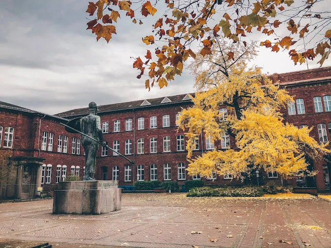 Karlsruhe Teknoloji Enstitüsü Tarihi Kampüs ve Sonbahar Manzarası Karlsruhe Teknoloji Enstitüsü, tarihi kırmızı tuğla binaları ve sanatsal heykelleriyle Almanya’nın en prestijli teknik üniversitelerinden biridir. Sonbaharın eşsiz renkleriyle süslenen kampüs alanı, öğrencilere huzurlu ve ilham verici bir eğitim ortamı sunar. Karlsruhe Teknoloji Enstitüsü’nün bu tarihi avlusu, hem akademik hem de kültürel yaşamın merkezinde yer alan ikonik bir noktadır.